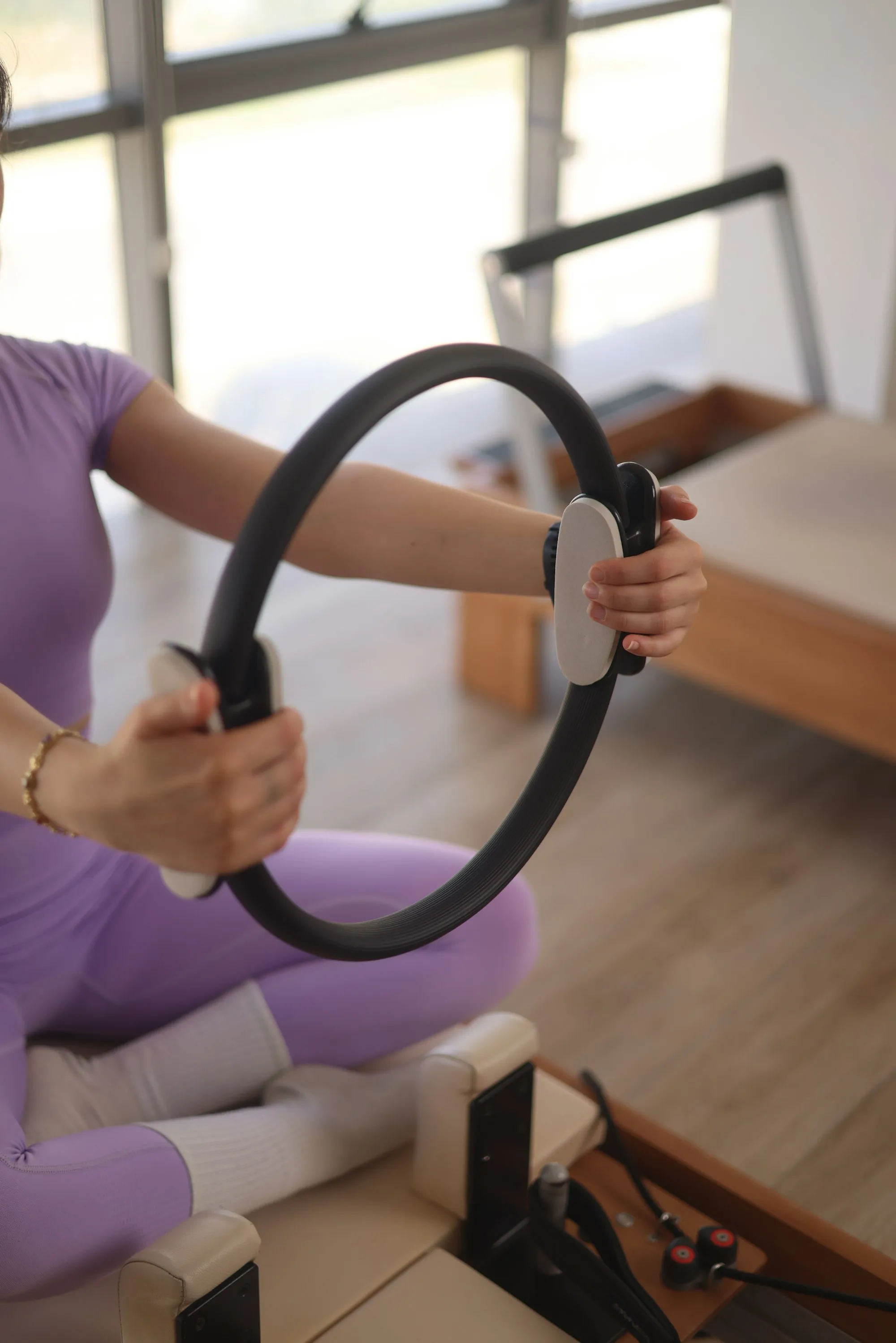 Woman working with a pilates ring while seated on a reformer
