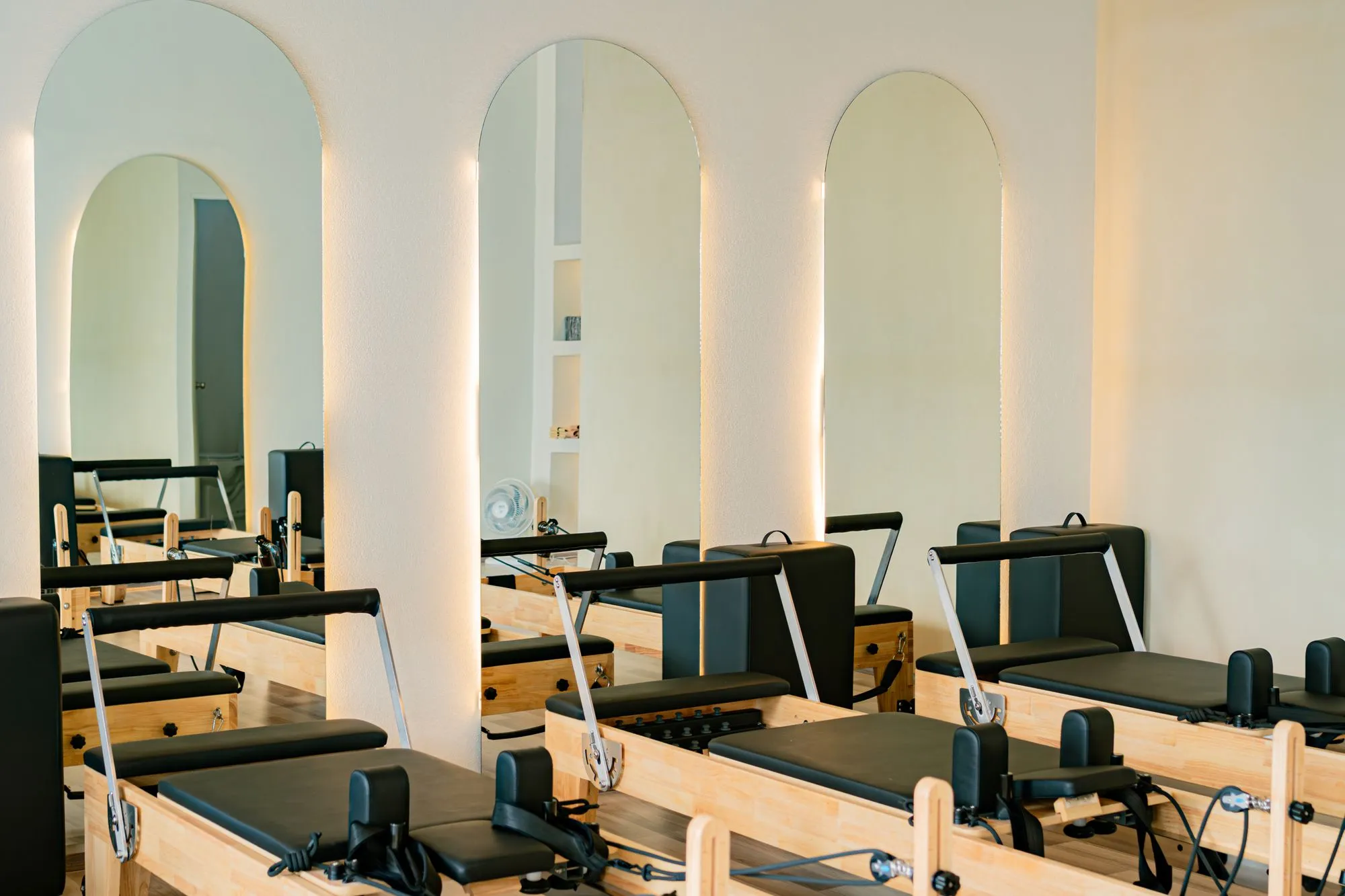 Empty studio with a row of wooden reformers and arched mirrors